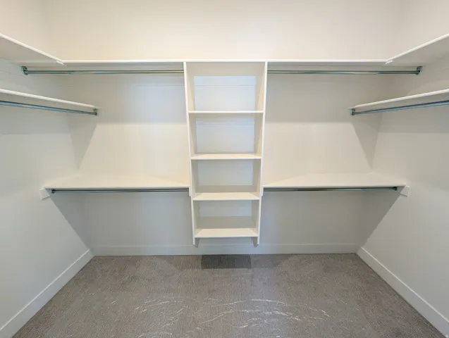 Walk-in closet featuring built-in shelving, multiple hanging rods, and light-colored carpeting