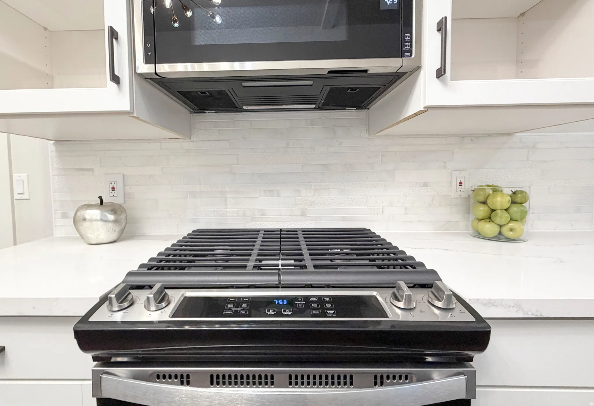 Stainless steel convection gas range with coordinating microwave, white cabinetry, backsplash, and quartz countertops