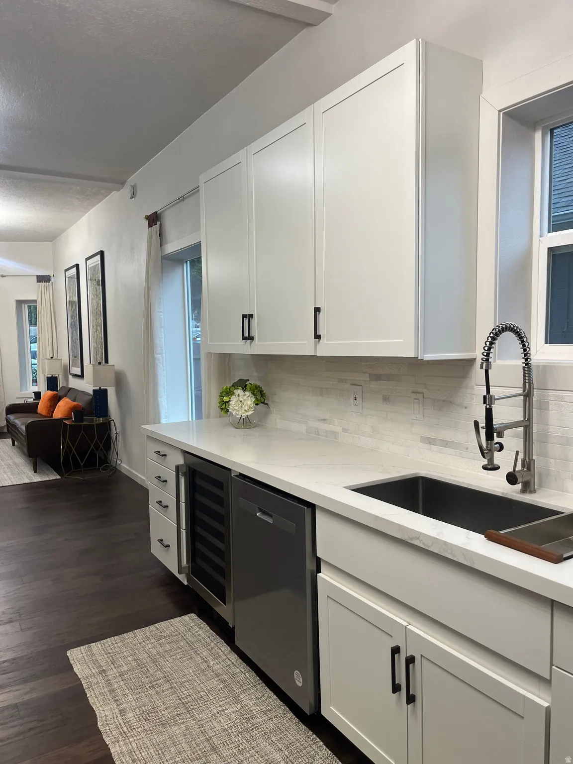 White shaker cabinetry with matte black hardware, integrated stainless steel dishwasher, wine refrigerator, single basin farmhouse sink, and a pull-down faucet