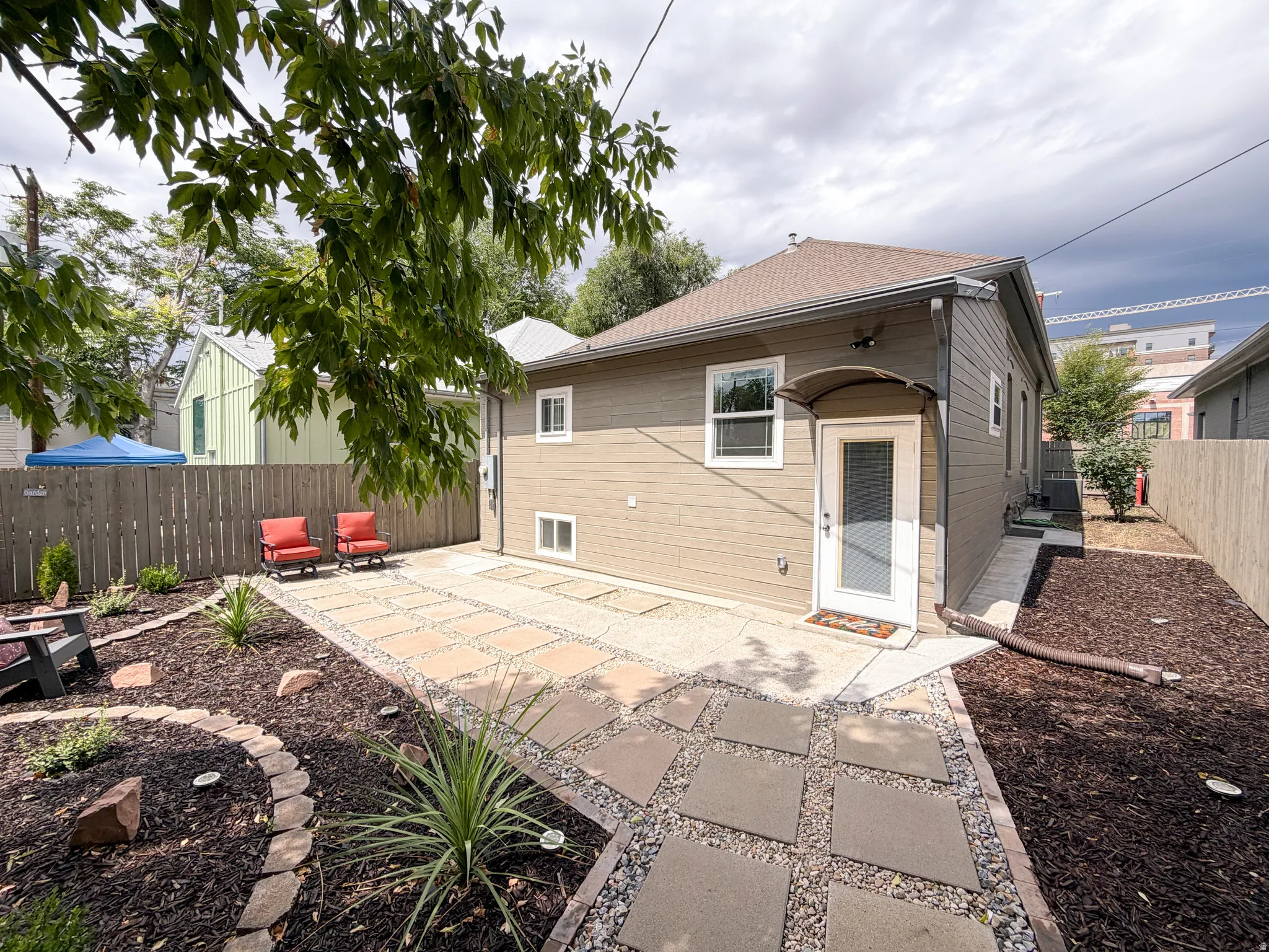Landscaped yard with stone pavers and gravel pathway, privacy fence, and a covered entryway.