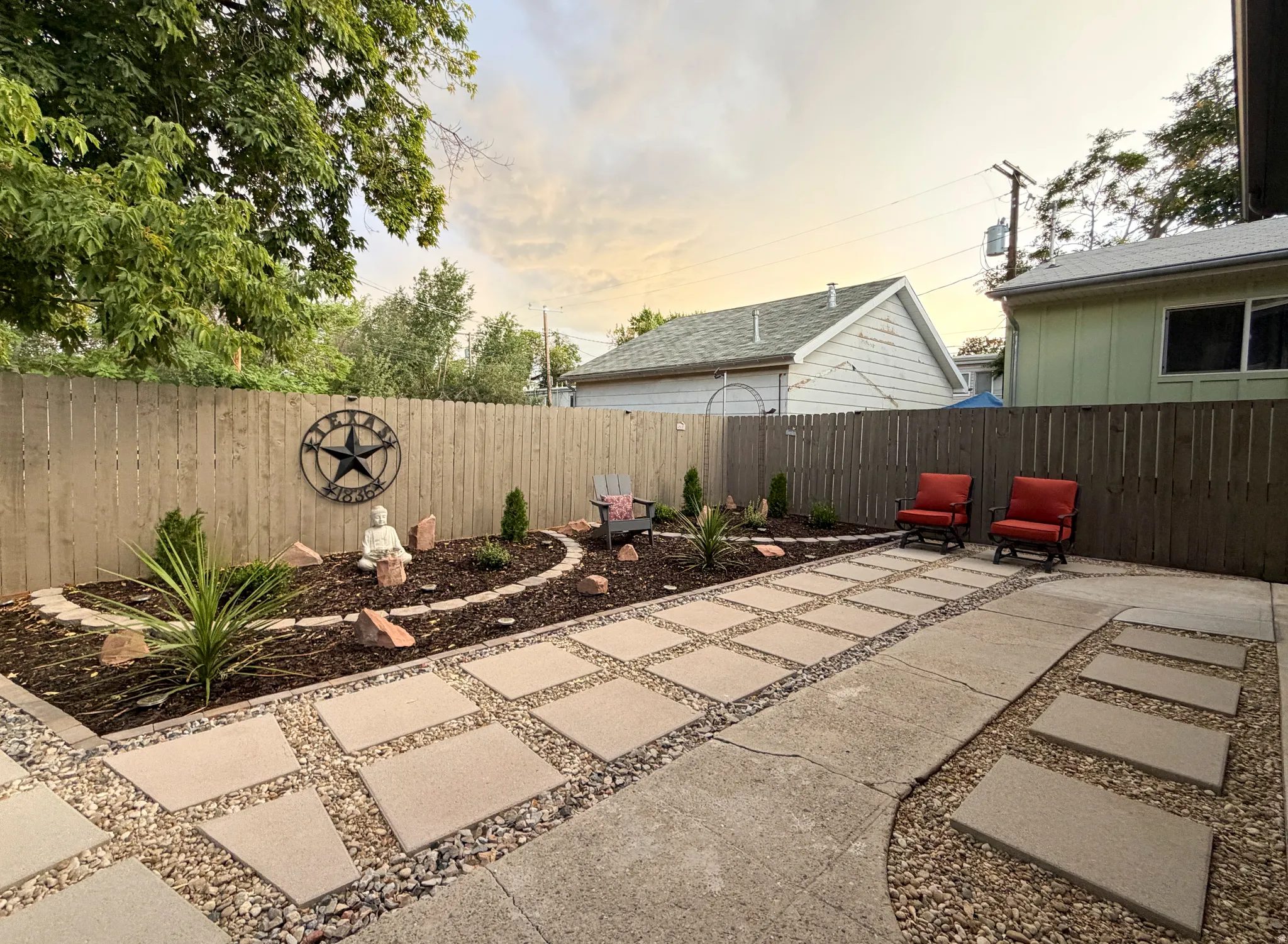 Fenced, private backyard featuring concrete paver patio, with low-maintenance garden beds and decorative rocks