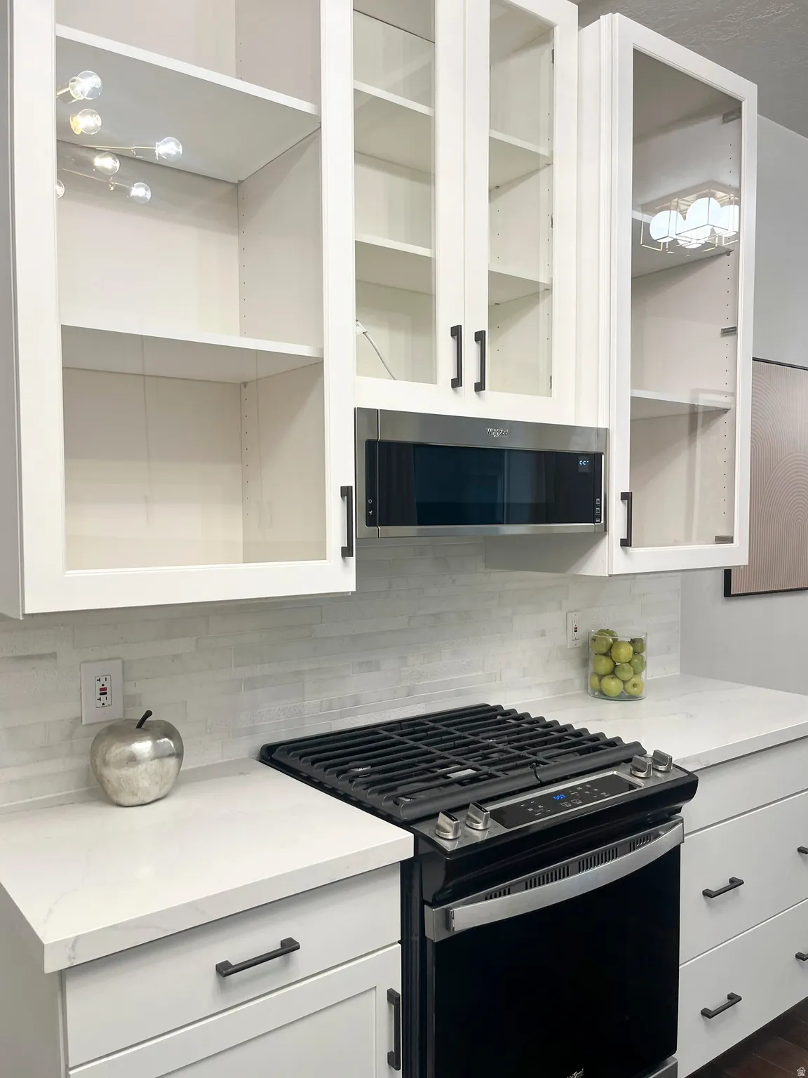 Quartz countertops, tile backsplash, and stainless steel gas range with overhead designer microwave.