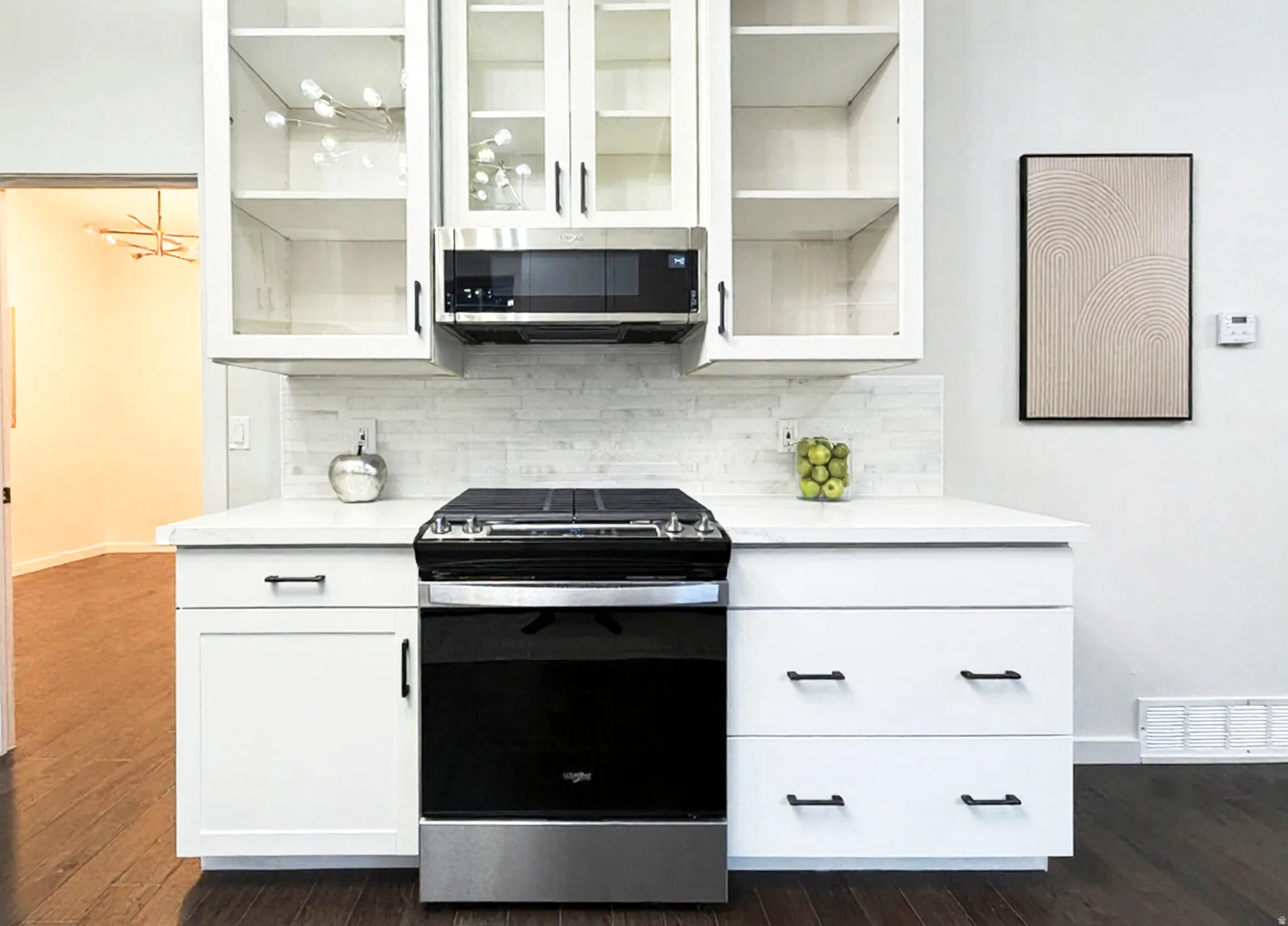 Glass-front upper doors, backsplash, stainless steel microwave, and gas range.