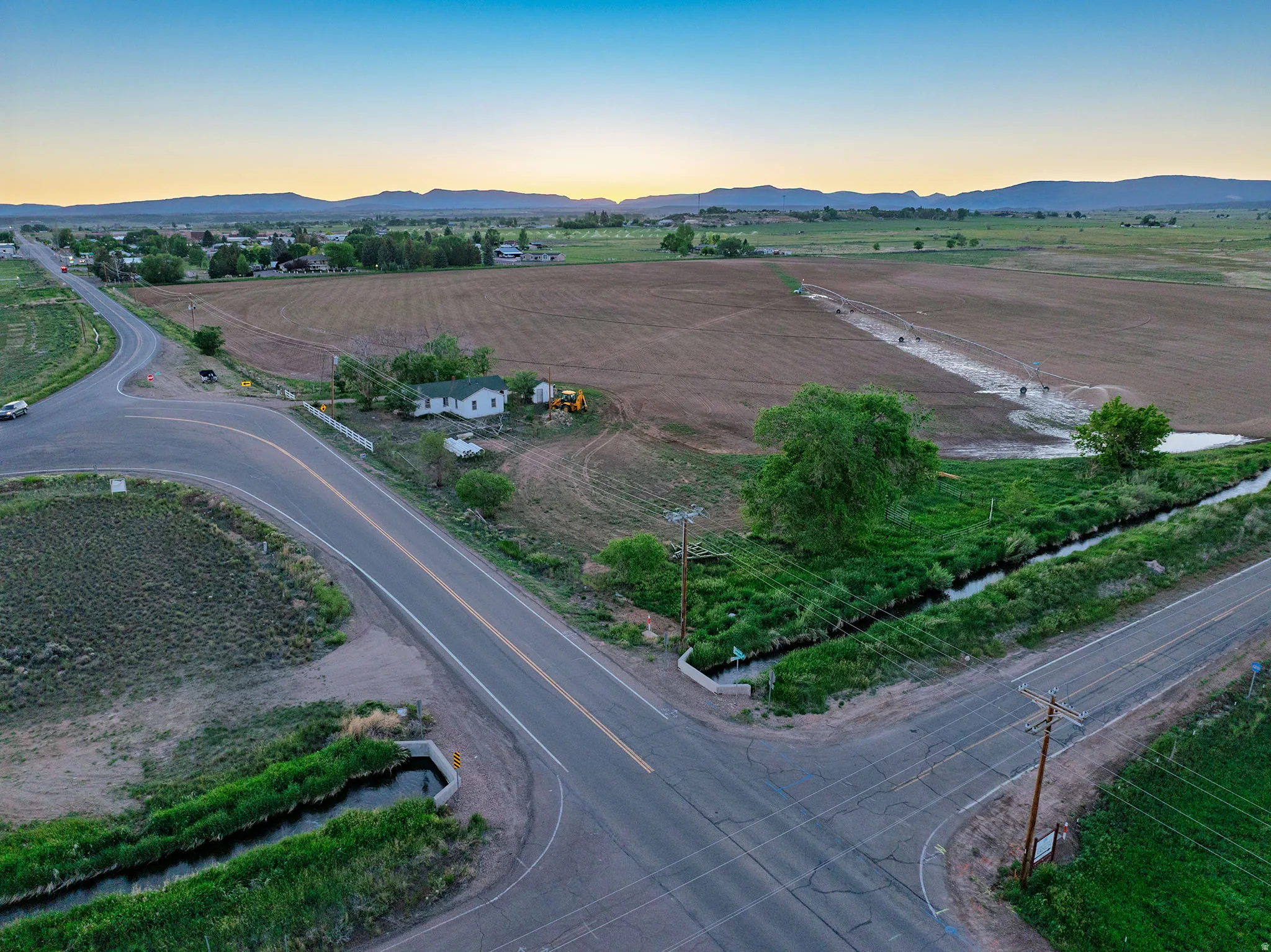 Rural property featuring a white single-story residence with a green roof, set against expansive agricultural fields