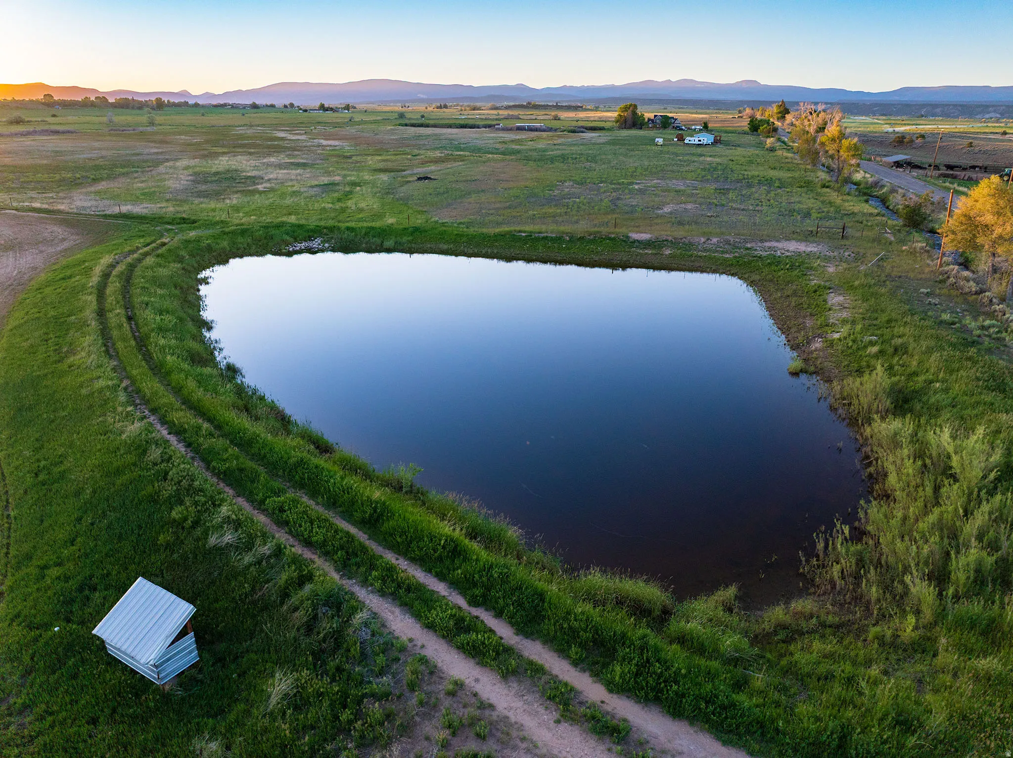 Expansive pond with tranquil water, surrounded by green grass and a dirt track