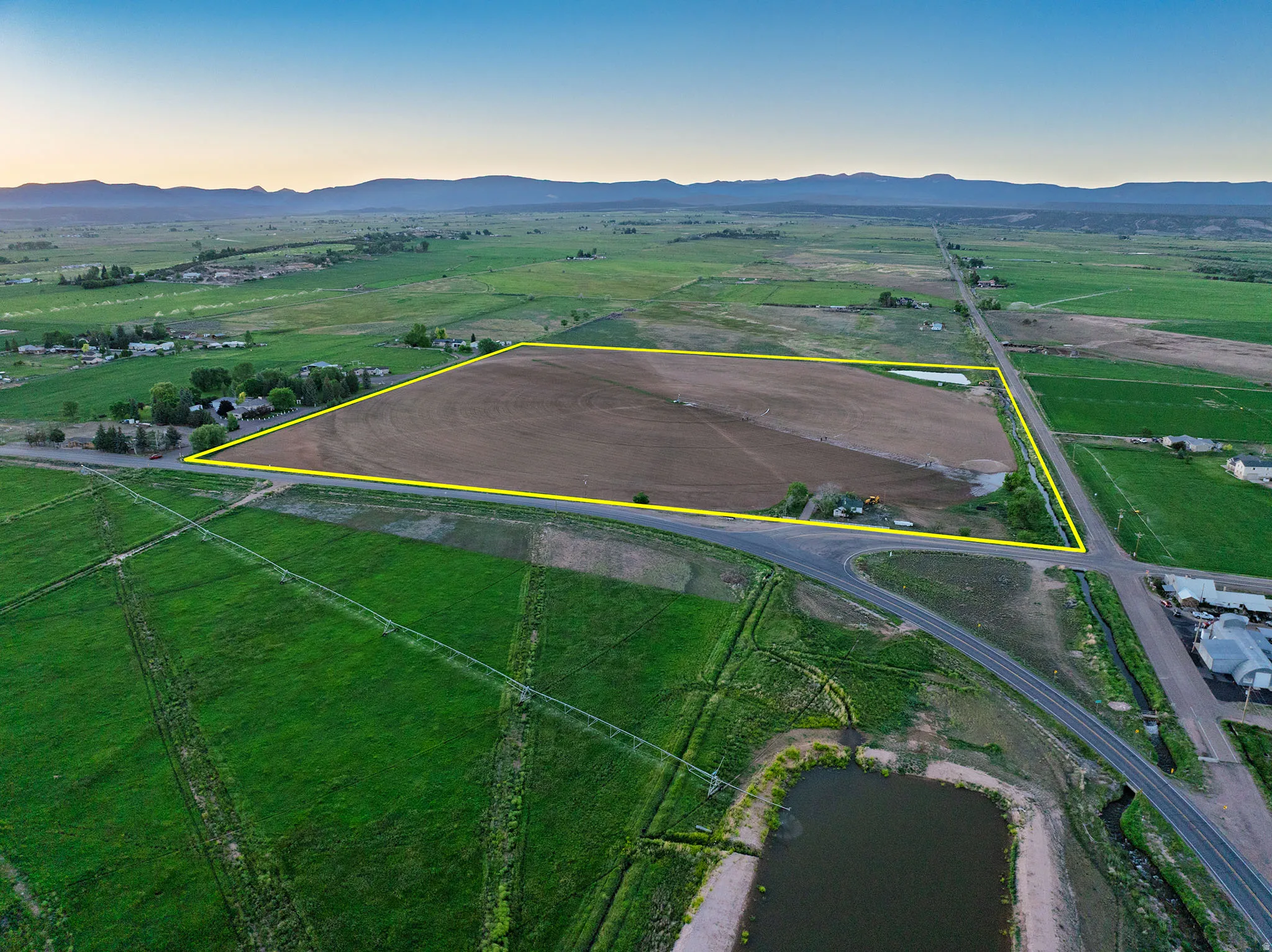 Expansive agricultural land featuring a tilled field, bordered by established roads and distant mountain ranges
