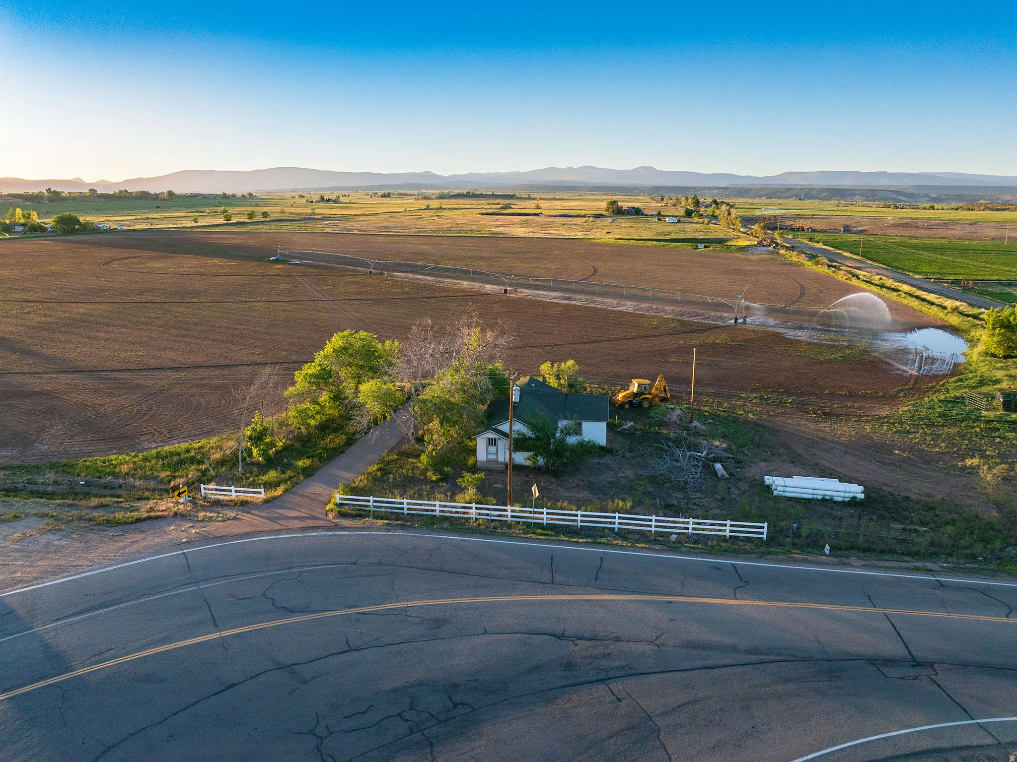 Expansive agricultural land featuring a single-family residence, mature trees, and a white picket fence