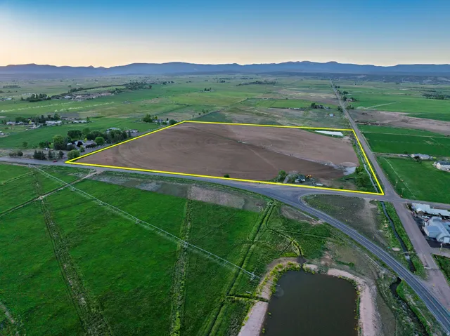 Expansive agricultural land featuring a tilled field, bordered by established roads and distant mountain ranges