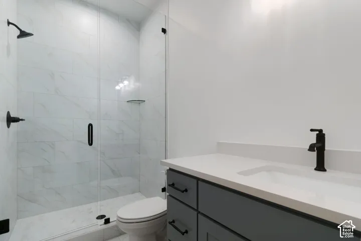 Glass-enclosed shower with a black shower head and handle, white tile surround, and a corner shelf