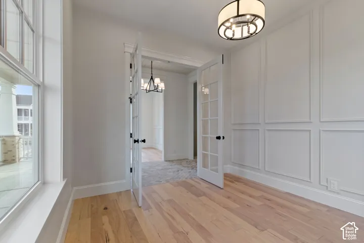 Hardwood flooring, French doors, detailed wall paneling, a drum pendant light fixture, and tall windows