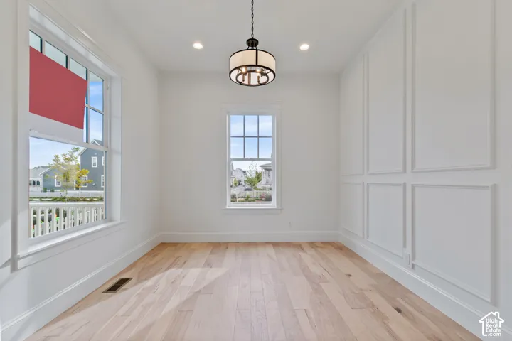 Light wood-finish flooring, recessed lighting, and a drum-style chandelier illuminate this room with decorative wall molding