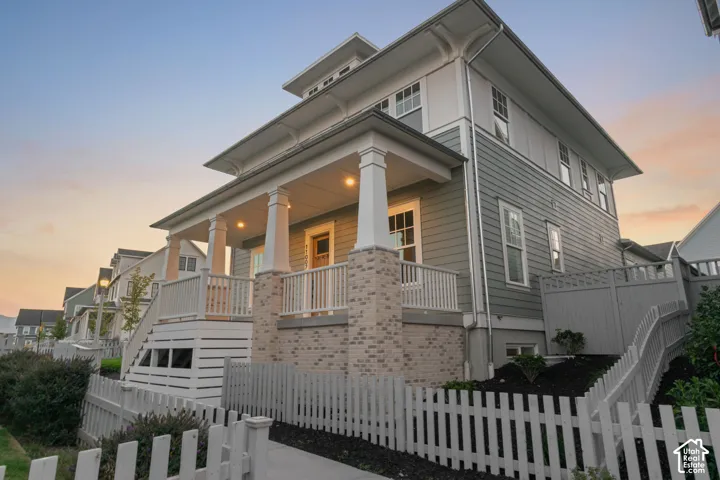 Multi-story residence featuring light gray siding with white trim, a covered porch with substantial columns, and a white picket fence