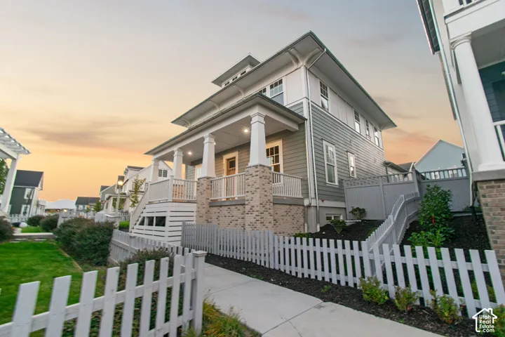 Craftsman-style residence featuring a prominent covered porch with substantial columns, brick detailing, and a white picket fence