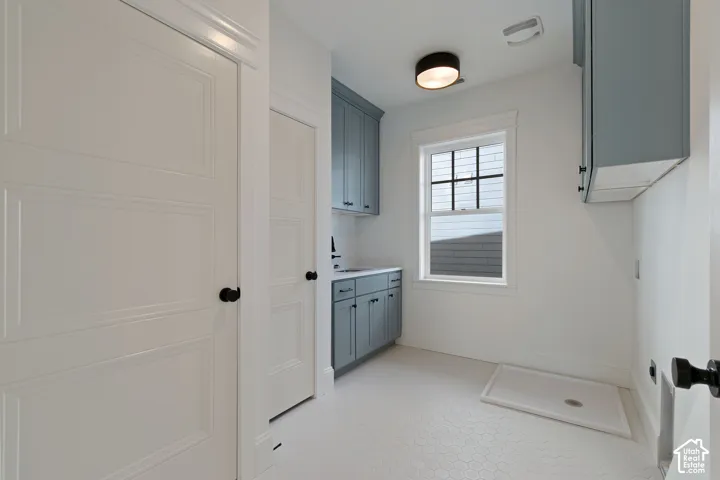 Recessed panel doors, hexagon tile flooring, light blue cabinetry, countertop with integrated sink, and overhead illumination