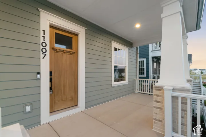 Covered front porch featuring white columns with brick accents, gray siding, a wood-finish front door, and recessed lighting