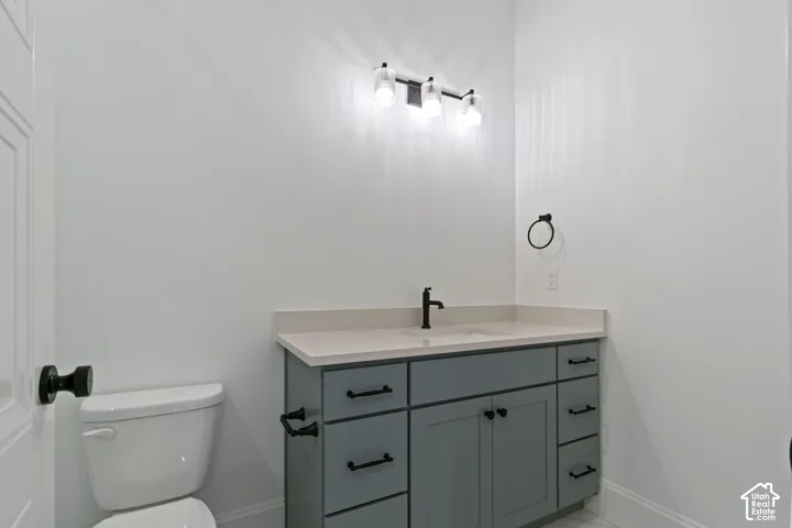 White toilet, gray vanity with countertop, rectangular sink, matte black faucet, and three-light vanity fixture