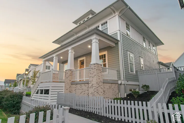 Exterior featuring a covered porch with white columns, light brick accents, horizontal siding, vertical siding, and a white picket fence