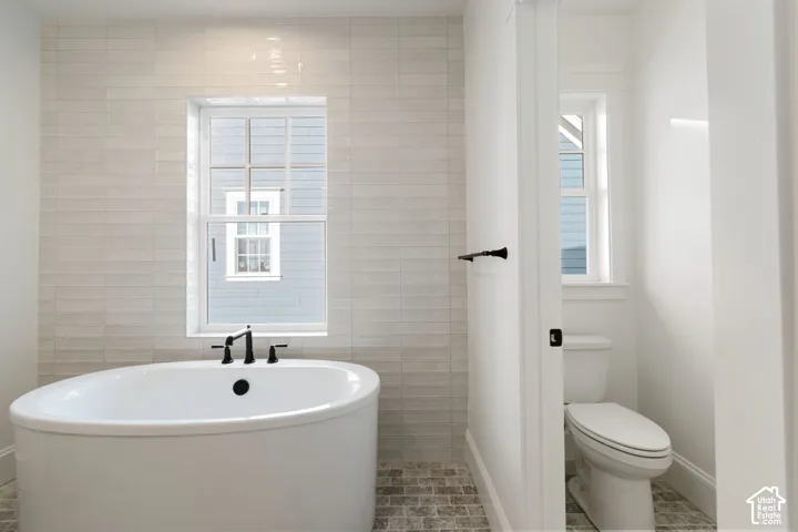 Freestanding oval bathtub with matte black fixtures, set against a tiled accent wall and window, complemented by mosaic floor tiling