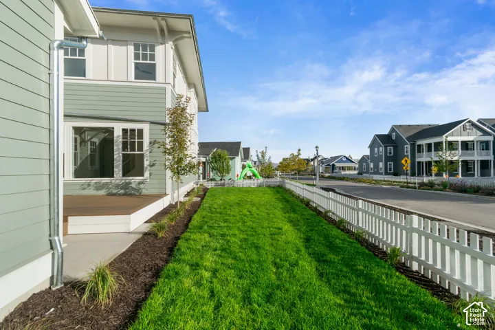 Exterior siding with white trim, wood-finish decking, and a manicured lawn featuring a white picket fence
