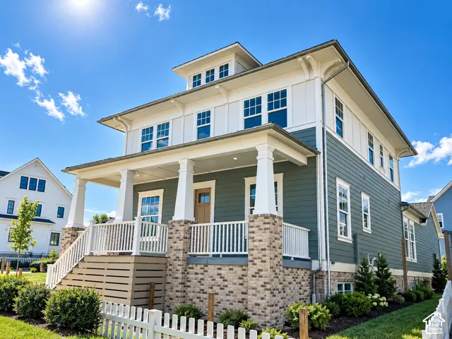Exterior featuring a covered porch, brick foundation, light blue siding, white trim, and multiple windows