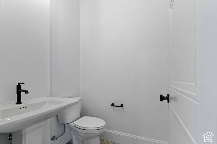 Pedestal sink with a matte black faucet, white toilet, and white panel door with black hardware