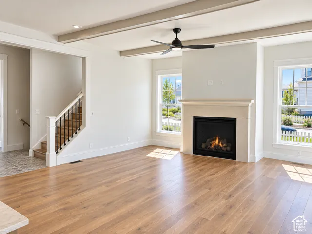 Wood-finish flooring, staircase with white newel posts and black balusters, integrated gas fireplace with stone-finish mantel, and ceiling fan with integrated lighting