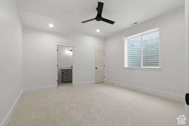 Spacious room featuring light-toned carpeting, a window with a window well, and a ceiling fan