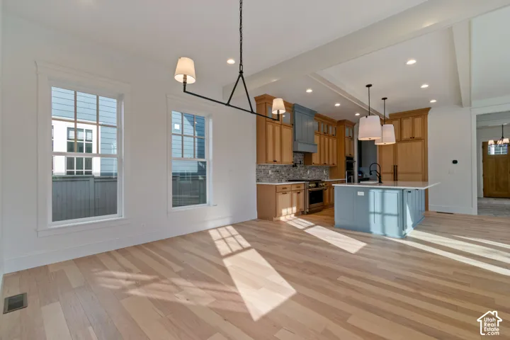 Hardwood-style flooring throughout, kitchen island with built-in sink and pendant lighting, recessed ceiling lights, white trim, and exposed ceiling beams