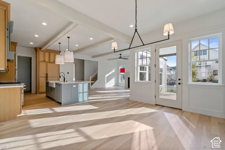 Light wood-finish flooring throughout, a kitchen island with an integrated sink, shaker-style cabinetry, recessed lighting, and a glass-paneled exterior door