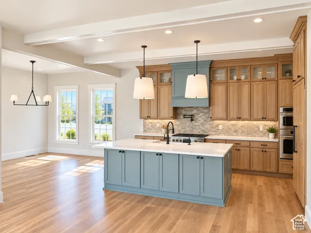 Spacious kitchen featuring a central island with a solid surface countertop, light wood-finish flooring, two-tone cabinetry, and a tile backsplash