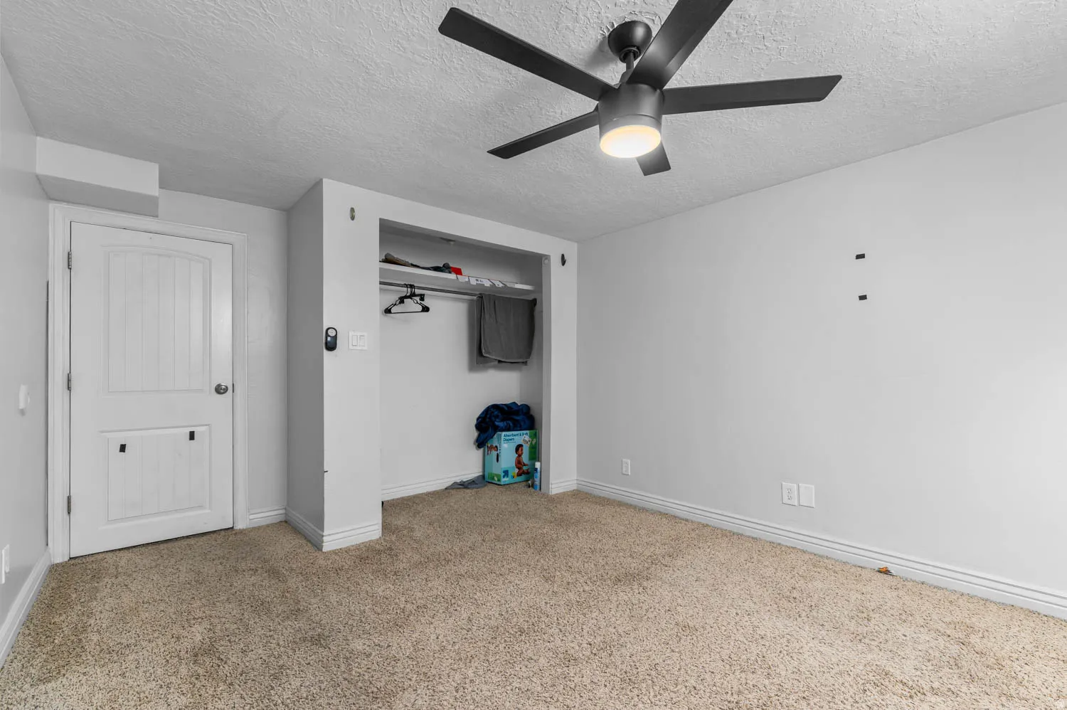 Room with textured carpet flooring, a white paneled door, and an open closet