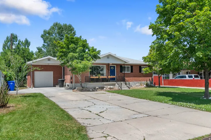 Brick exterior residence with an attached garage, a paved driveway, and mature landscaping