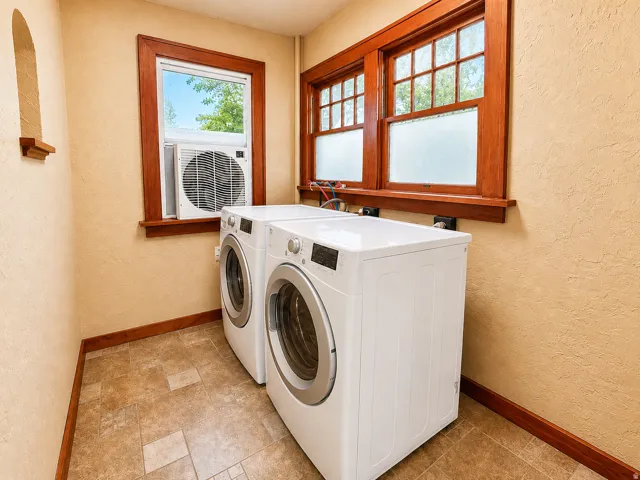 Dedicated utility space featuring a washer and dryer set, two multi-pane windows with wood trim, an additional window with wood trim, a built-in wall niche, and tile flooring