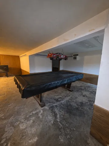 Finished basement space featuring concrete flooring, wood paneling, and an exposed beam ceiling