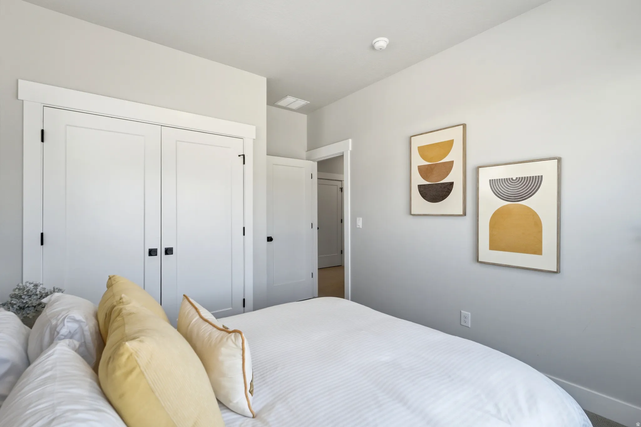 Spacious bedroom featuring light gray walls, white trim, and a white double-door closet with black hardware