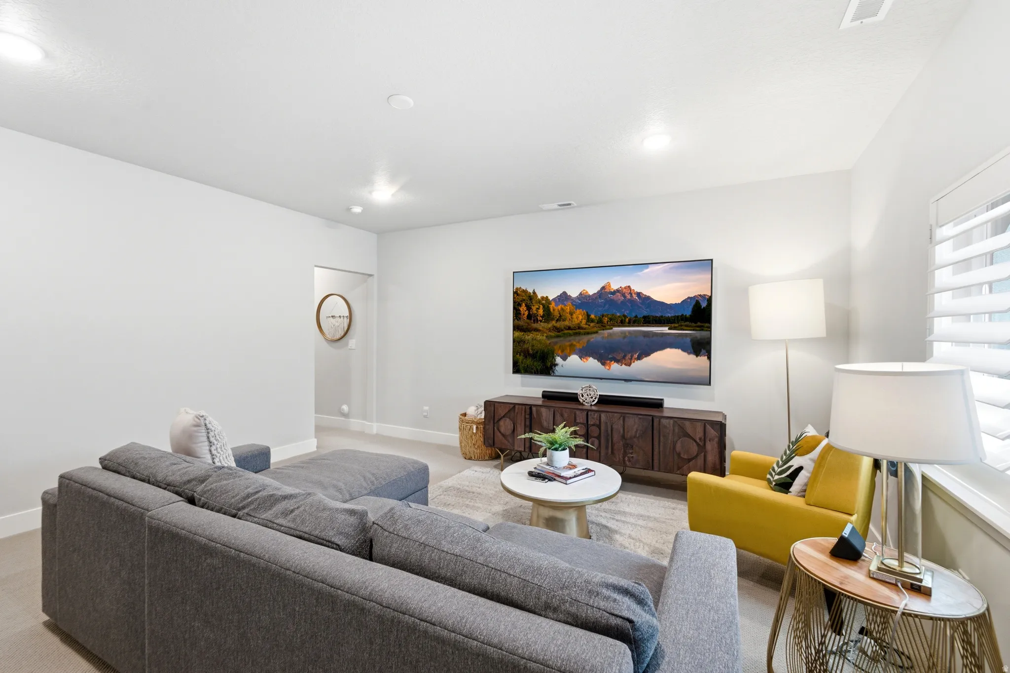 Spacious living area featuring neutral wall tones, recessed lighting, a large window with white plantation shutters, and light-toned carpeting