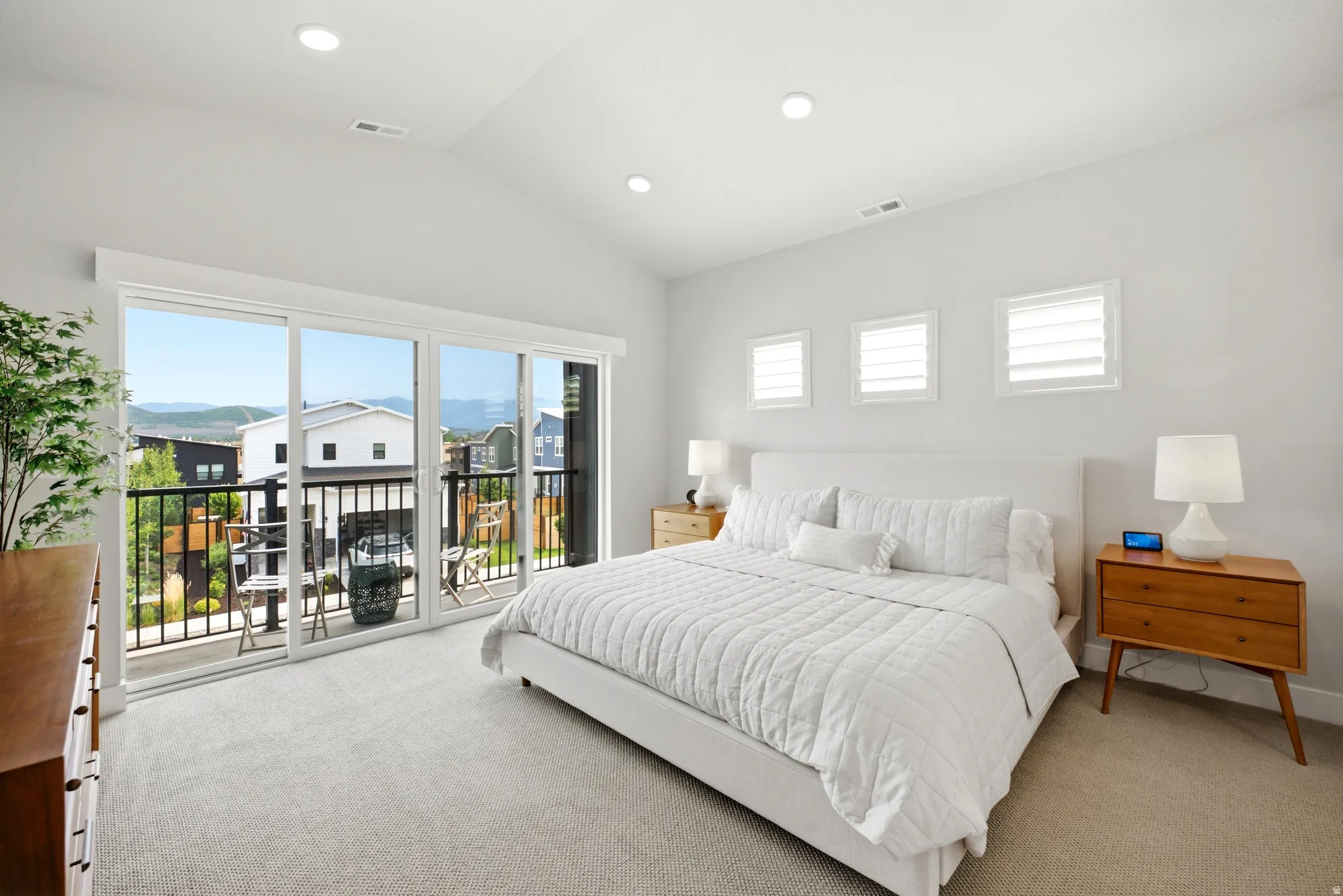 Spacious bedroom featuring vaulted ceilings, recessed lighting, expansive sliding glass doors opening to a balcony with mountain scenery, and three transom windows