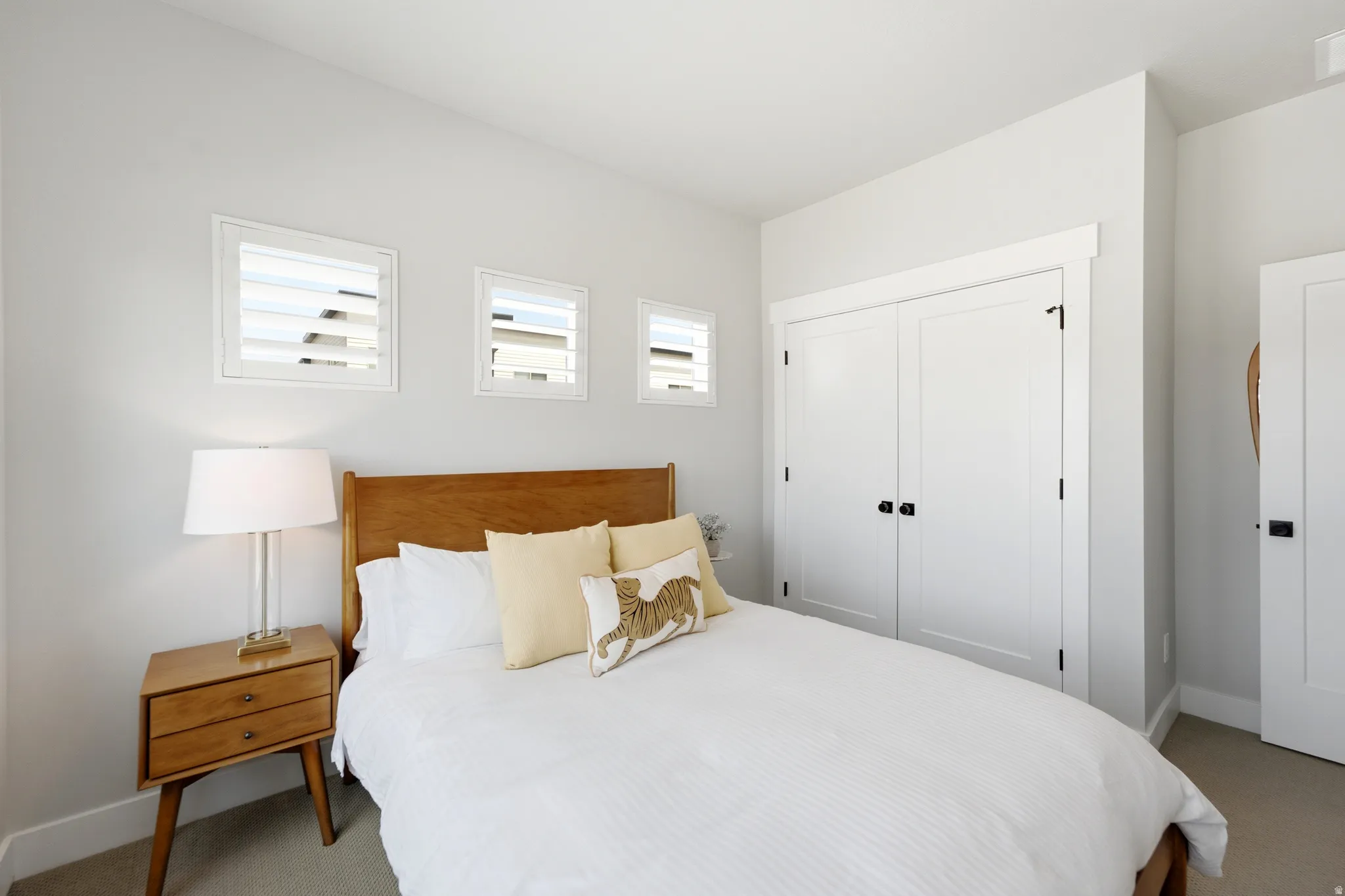 Bedroom featuring three horizontal windows with white plantation shutters, a wood-finish headboard, white bi-fold closet doors with black hardware, and an additional white door with black hardware