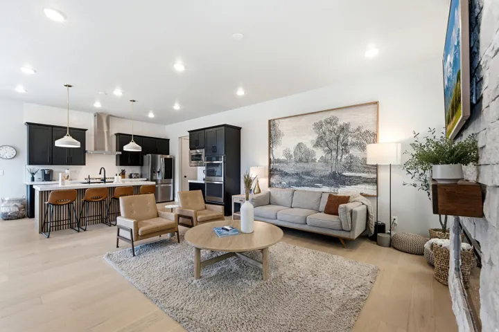 Open-concept living space featuring light wood-finish flooring, recessed lighting, and a kitchen with dark cabinetry, stainless steel appliances, and a breakfast bar island with pendant lighting