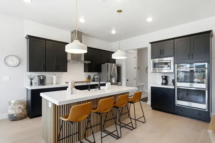 Modern kitchen featuring black cabinetry, a white subway tile backsplash, and light wood-finish flooring