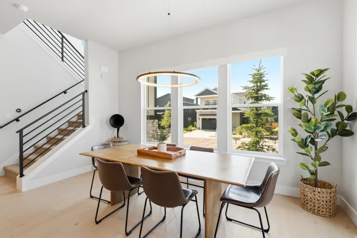 Bright dining area featuring large picture windows, wood-finish flooring, a contemporary circular pendant light, and an open staircase with a black metal railing