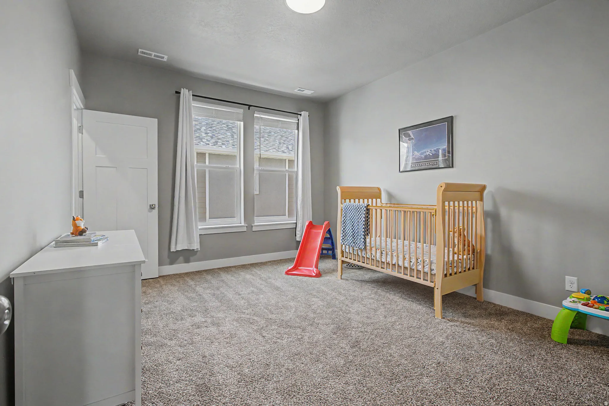 Spacious room featuring neutral carpeting, light gray walls, two bright windows with white trim, and a contemporary white door with panel detailing