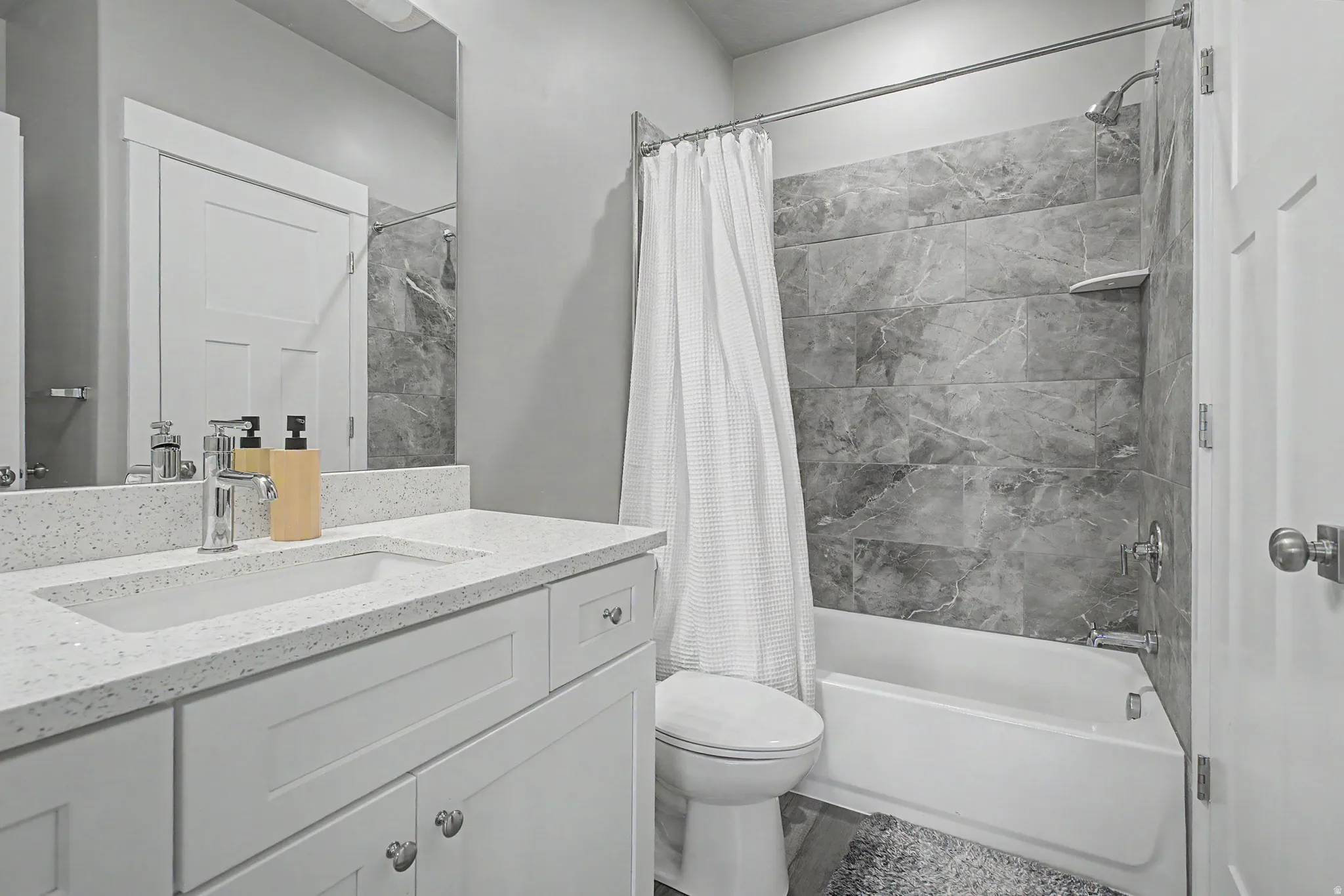 Bathroom featuring a white vanity with an integrated sink, a speckled countertop, and a large wall mirror