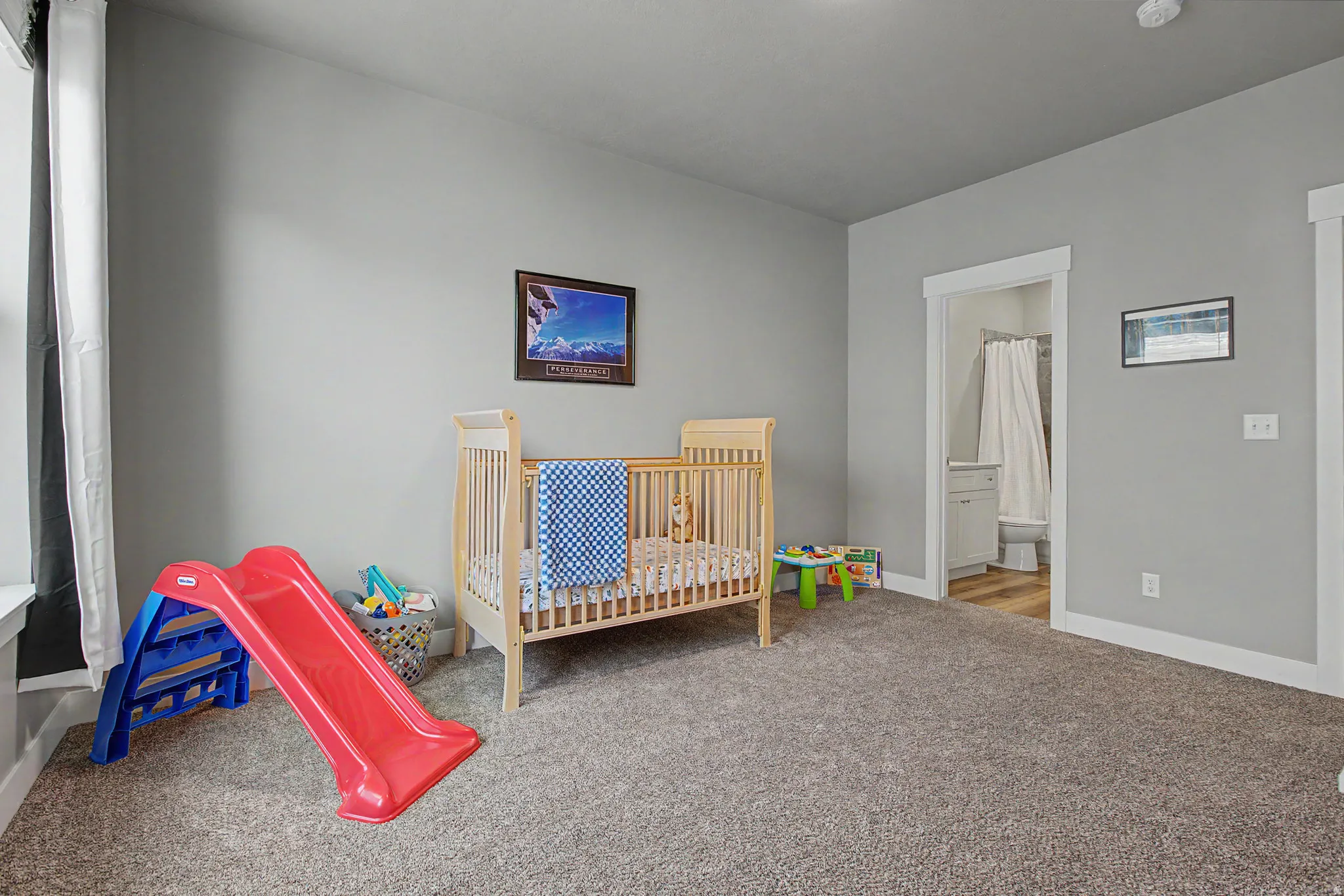 Spacious room featuring neutral gray walls, plush gray carpeting, and white baseboards