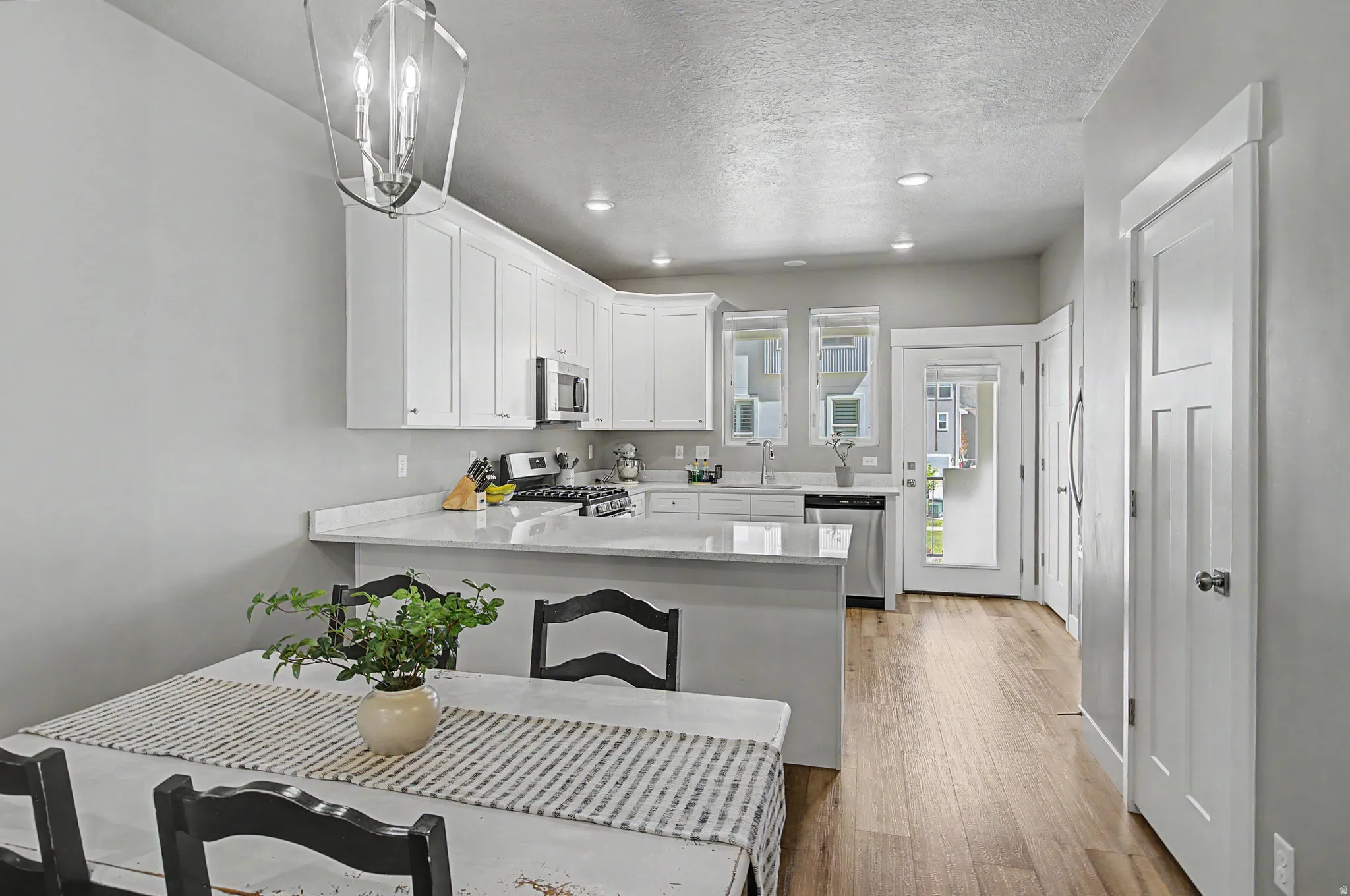 Kitchen area featuring white cabinetry, stainless steel appliances, light-toned countertops, and wood-finish flooring