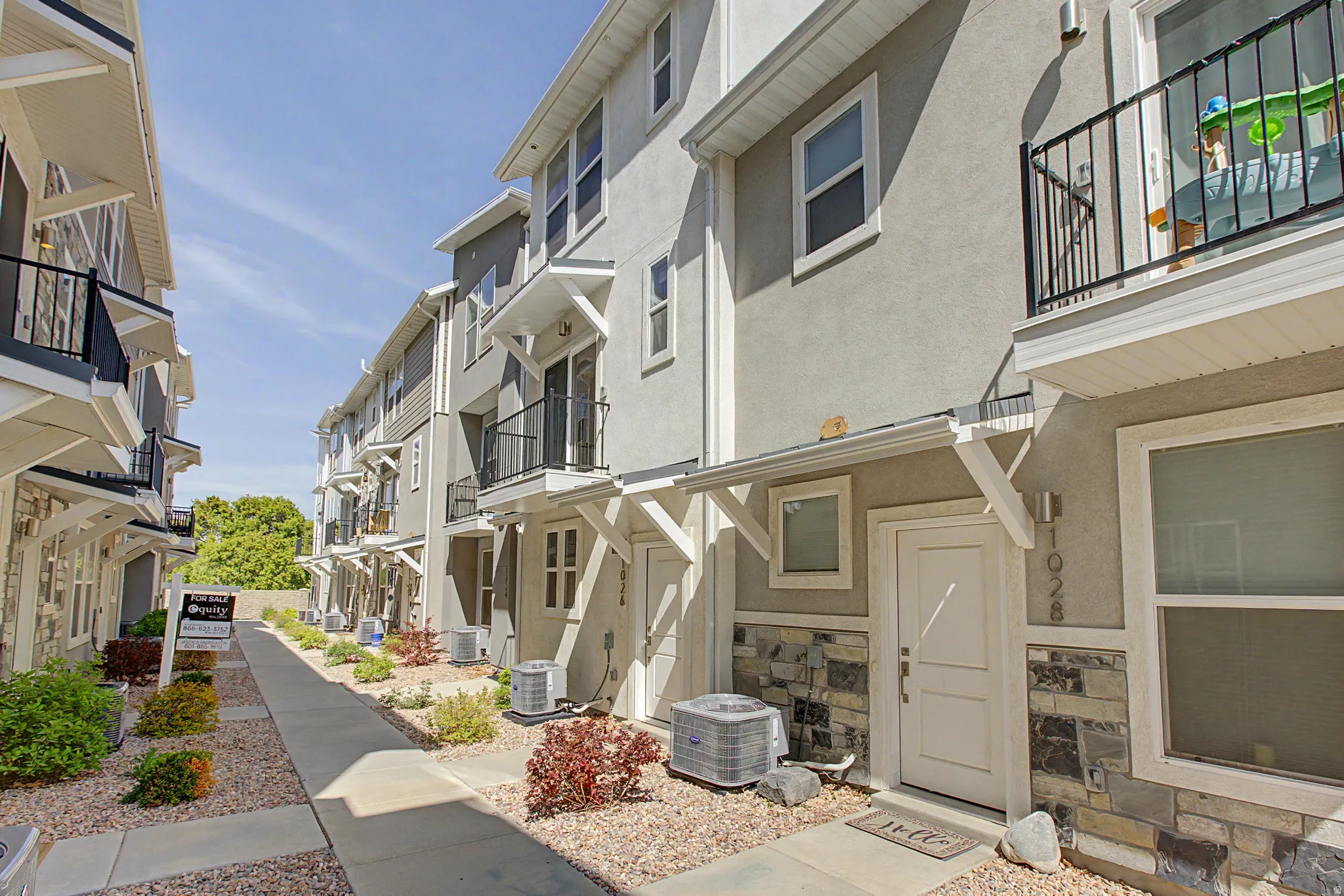 Contemporary multi-story facade featuring stucco siding, stone accents, multiple balconies with metal railings, and individual entryways