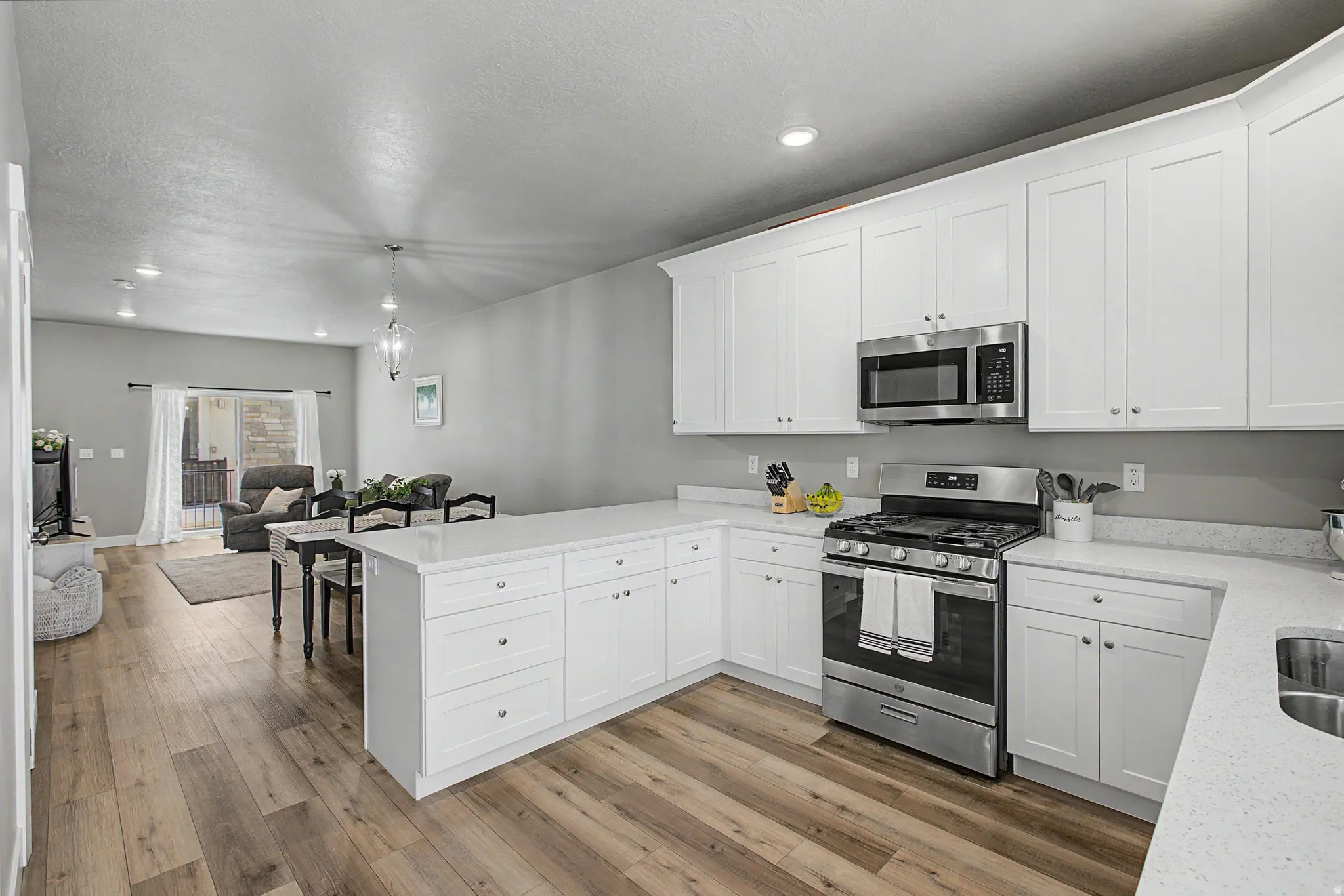Modern kitchen featuring white shaker cabinetry, stainless steel appliances, light-toned countertops, wood-finish flooring, and recessed lighting