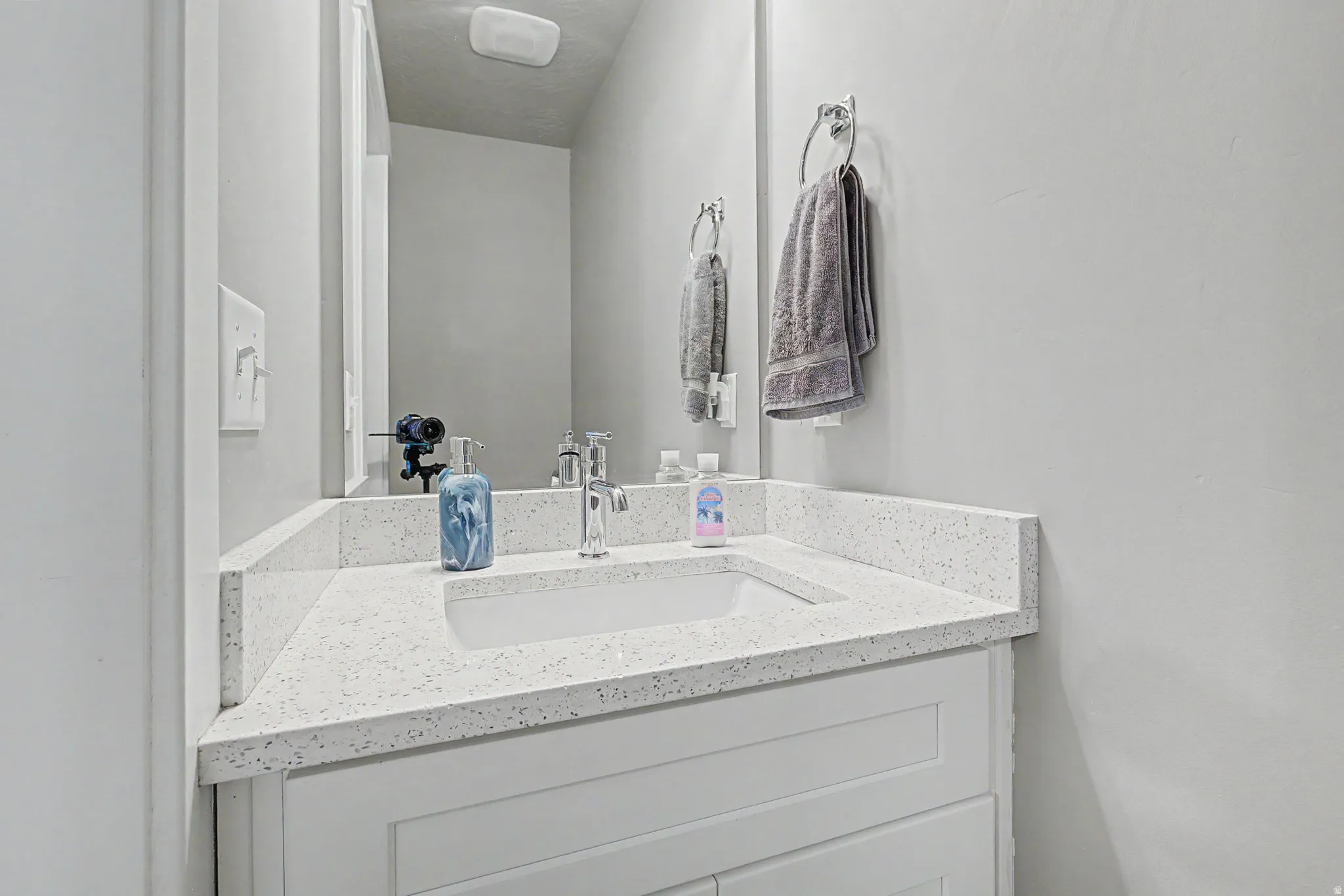 White vanity with an integrated sink, speckled countertop, chrome faucet, and mirrored wall