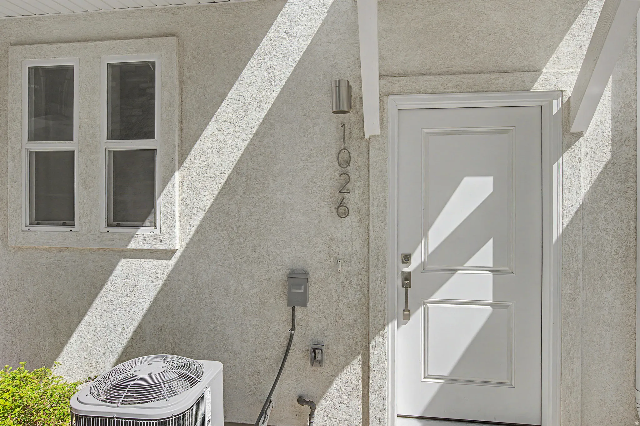 Textured stucco exterior featuring a paneled entry door with brushed nickel hardware, an exterior sconce, and white-framed windows