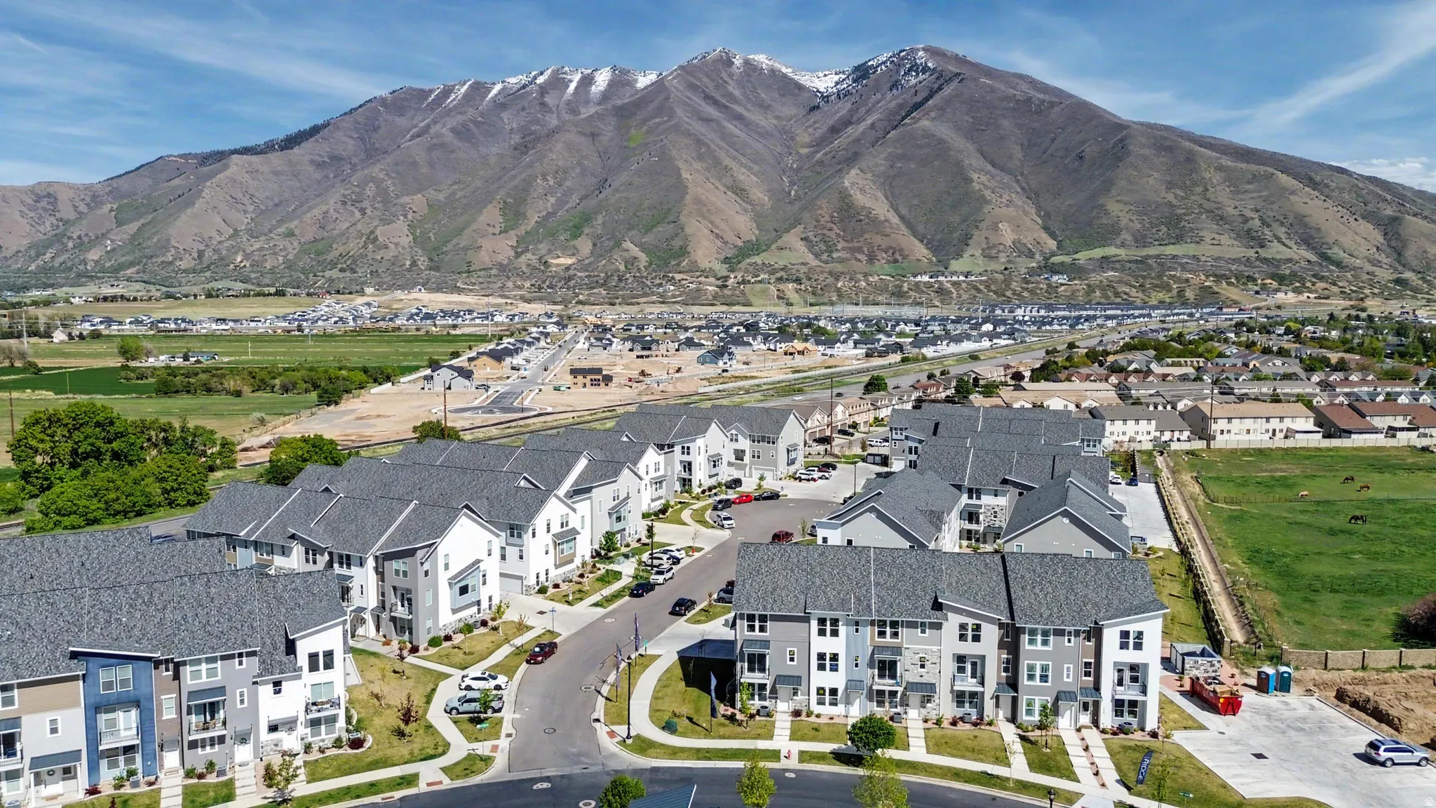 Modern residential development with a mountainous backdrop, featuring multi-story units, paved roadways, and landscaped common areas